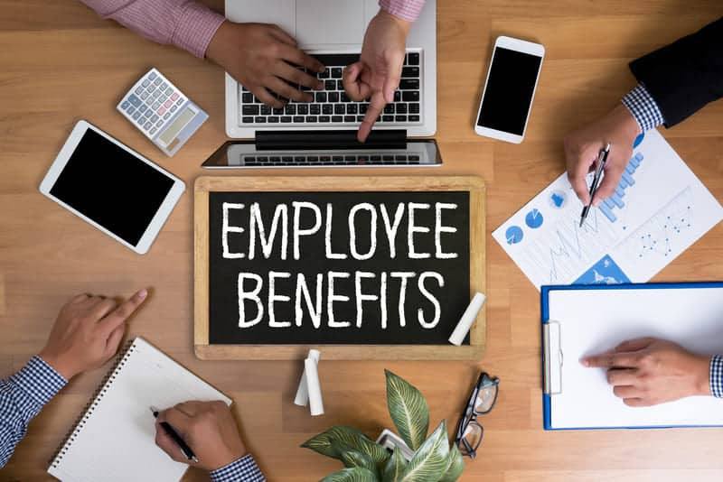 Employee benefits written on chalkboard surrounded by employees on table