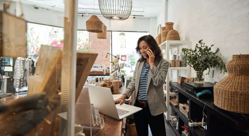 Business owner standing using a laptop while on the phone