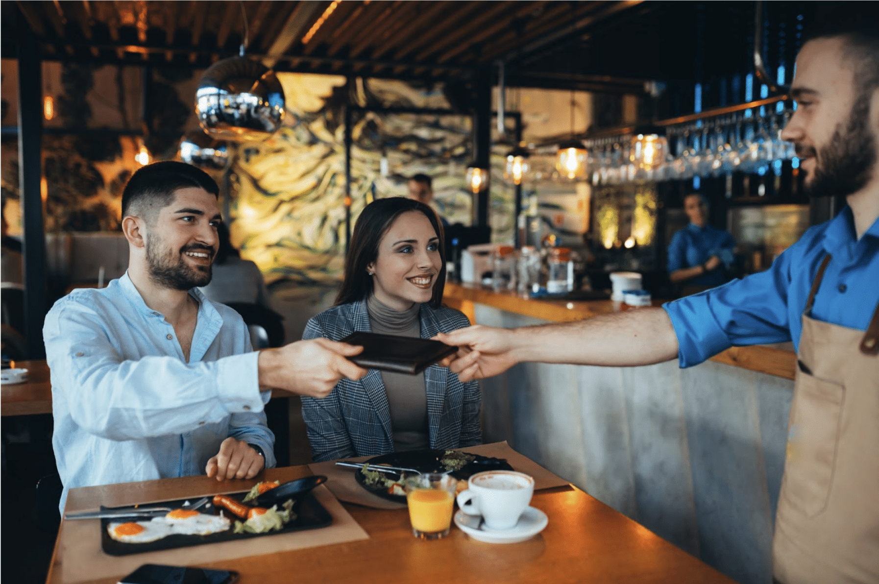 A couple paying their bill to a server after breakfast. Keywords: tip pooling, payroll considerations, gratuity, service charge, hospitality tipping models, digital tipping, customer experience, payroll compliance in restaurants.